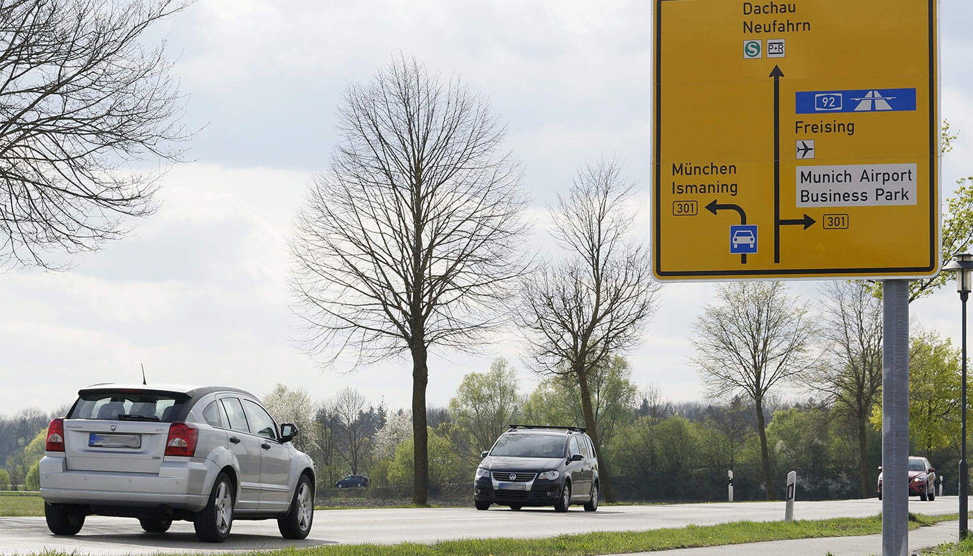 Anfahrt mit dem Auto Eine Bundestraße mit Auto und einem Straßenbild das Richtung Flughafen weist