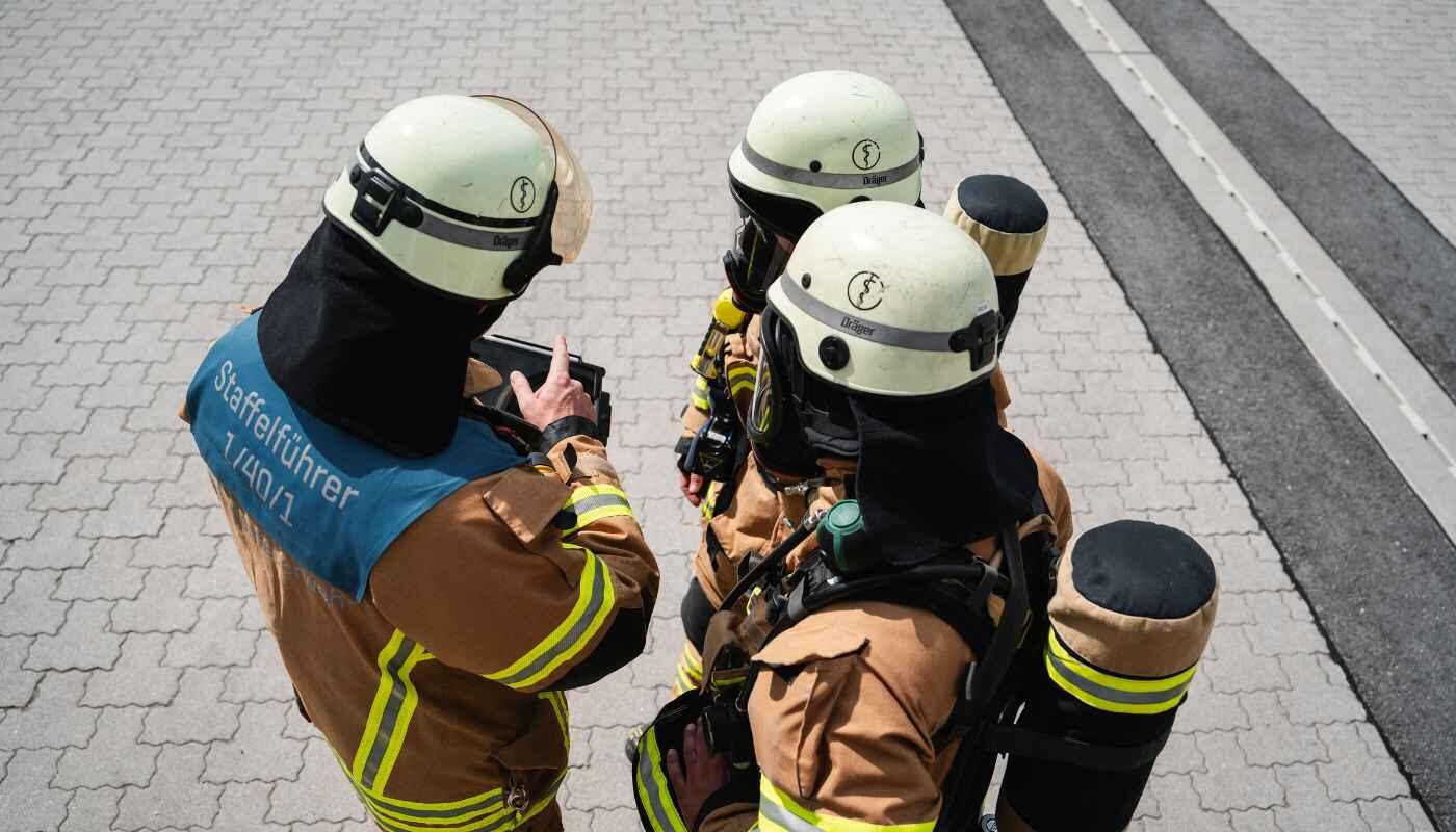Brandschutzmeister Brandschuztmeister bespricht sich mit zwei Feuerwehrleuten über Sicherheitsmaßnahmen und Feuerwehreinsätze