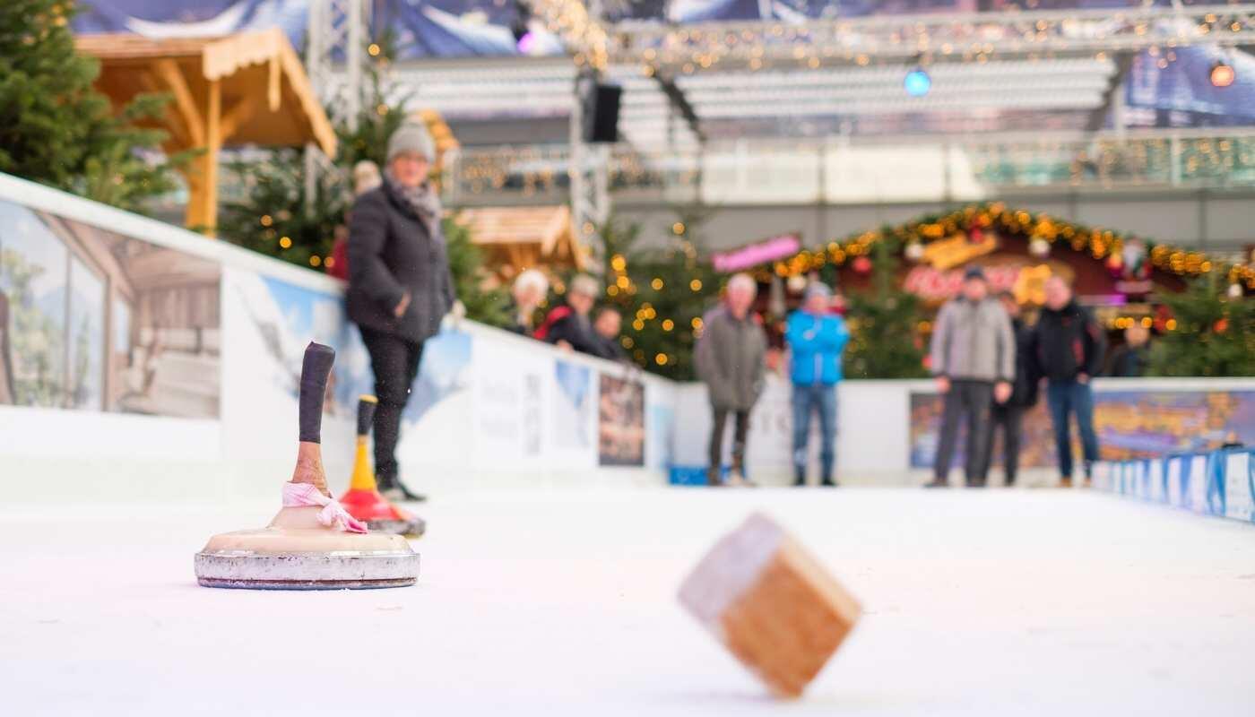 Weihnachts- und Wintermarkt 2024 Eisstockschießen auf unserem Wintermarkt: Zwei Eisstöcke im Vordergrund, im Hintergrund sind Menschen auf der Eisbahn zu sehen.