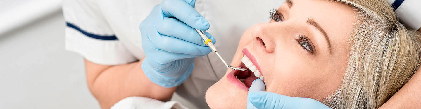 Zahnärztliche Behandlung am Flughafen München Nahaufnahme einer Patientin, die am Flughafen München auf einem Zahnarztstuhl liegt, während eine Zahnärztin mit Handschuhen ein zahnärztliches Instrument im Mundbereich verwendet; die Atmosphäre wirkt sauber, ruhig und vertrauensvoll.