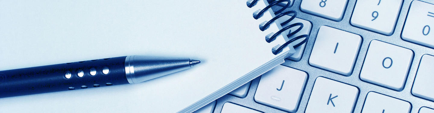 Press Release Close-up of a ballpoint pen and a spiral notepad next to a computer keyboard, representing the writing of press releases at Munich Airport; the scene appears calm, structured, and informative.