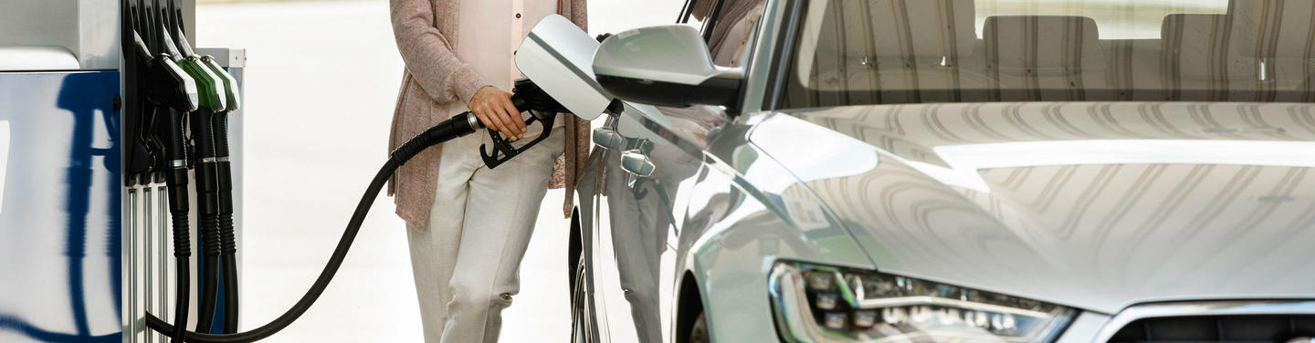 Fuel station service at Munich Airport A person stands next to a silver car holding a fuel nozzle while the vehicle is being refueled at a gas station at Munich Airport; the environment appears bright, modern, and calm.