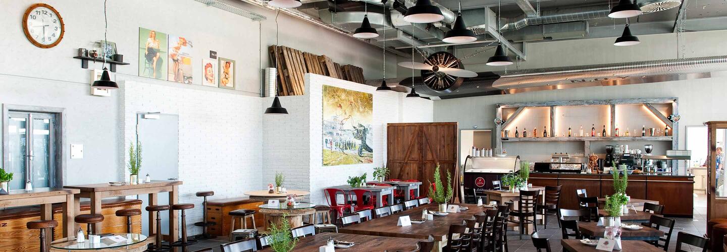 Location Tante Ju Heller, weitläufiger Restaurantbereich mit einer Mischung aus Holz, modernen Elementen und warmen Farbtönen. Geschmackvolle Pflanzen und stimmige Dekoration verleihen dem Tante Ju eine einladende, entspannte und hochwertige Stimmung.