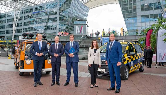 Das erste Bild zeigt den bayerischen Ministerpräsidenten, Dr. Markus Söder (3. von links), den FMG-Aufsichtsratsvorsitzenden Albert Füracker (links), Flughafenchef Jost Lammers (2. von links), die Geschäftsführerin Finanzen und Infrastruktur, Nathalie Leroy und den Geschäftsführer Commercial und Security, Jan-Henrik Andersson (rechts) vor einem historischen und einem modernen „Follow-Me“-Fahrzeug.