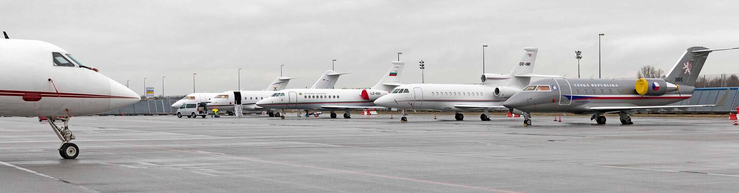 General Aviation on the Apron A row of business jets is parked on a wet airport apron under a grey, overcast sky, while ground staff work on one of the aircraft; the scene appears calm and operational.