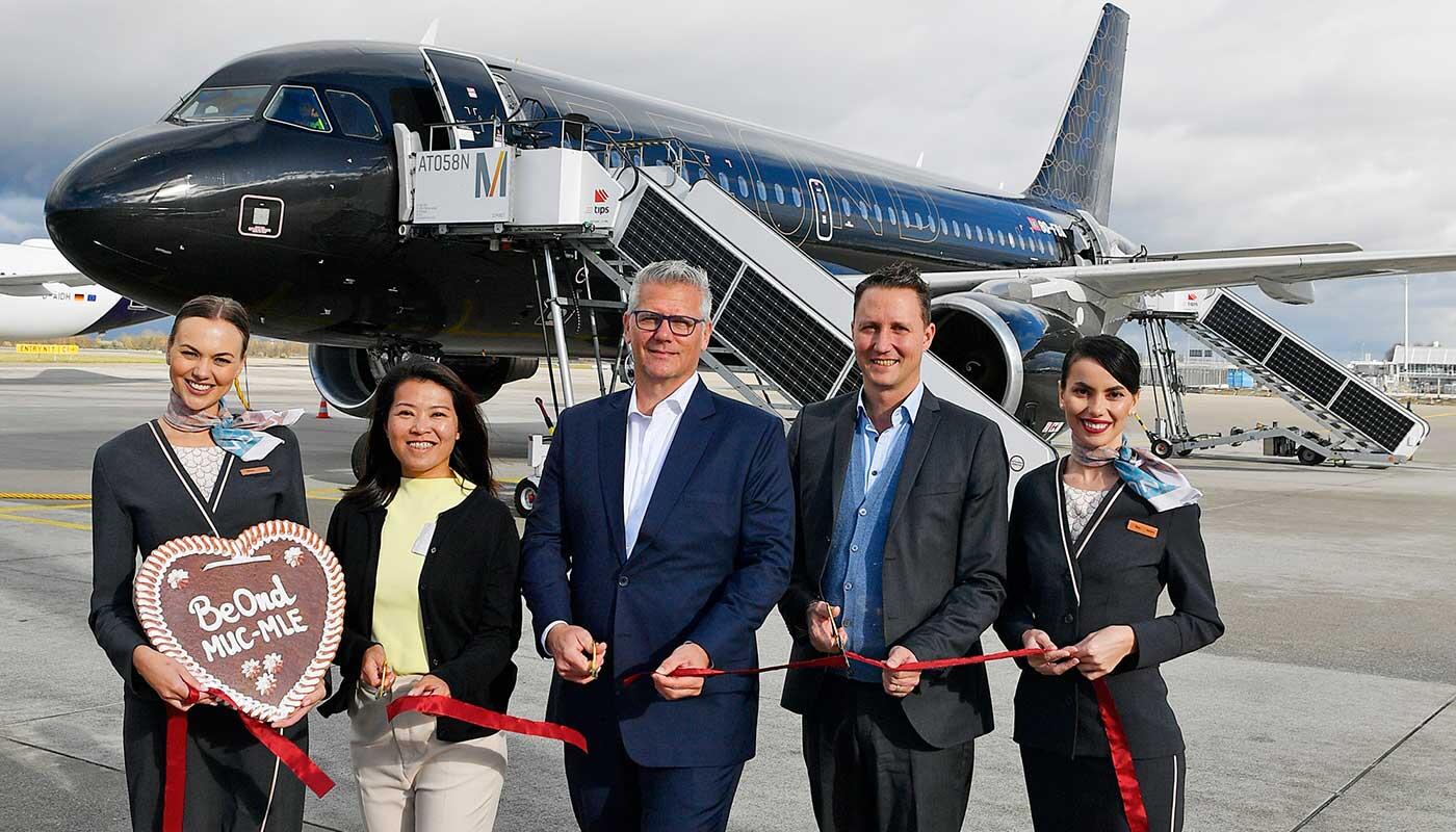 Erstflug der maledivischen Fluggesellschaft Beond Das Ribbon Cutting anlässlich des Erstfluges nach Male feierten - eingerahmt von der Beond Cabin Crew - Tiffany Koh (Head of Marketing and Communications von Beond), Sascha Feuerherd (Beond Chief Commercial Officer) und Oliver Dersch (Leiter des Geschäftsbereichs Aviation der Flughafen München GmbH) (v.l.n.r.)