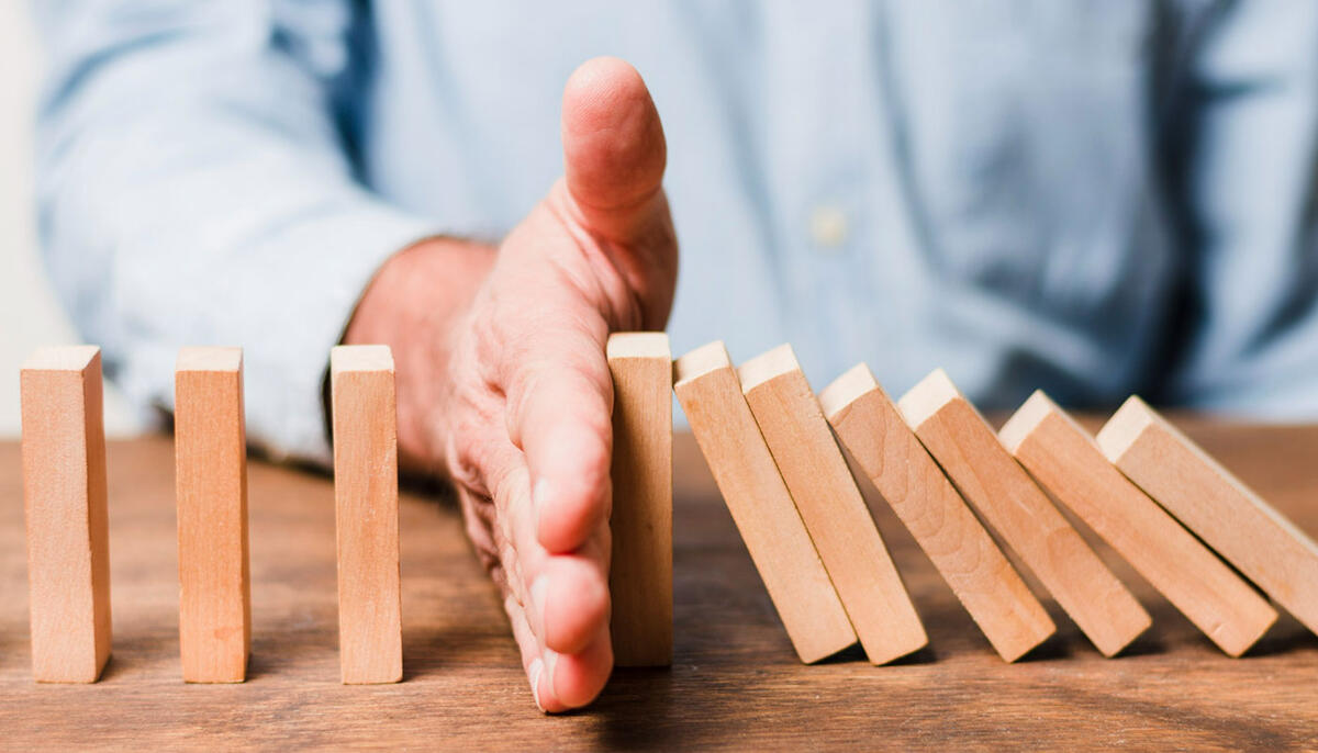 BCM Essentials Fallende Dominosteine, die von einer Hand gestoppt werden