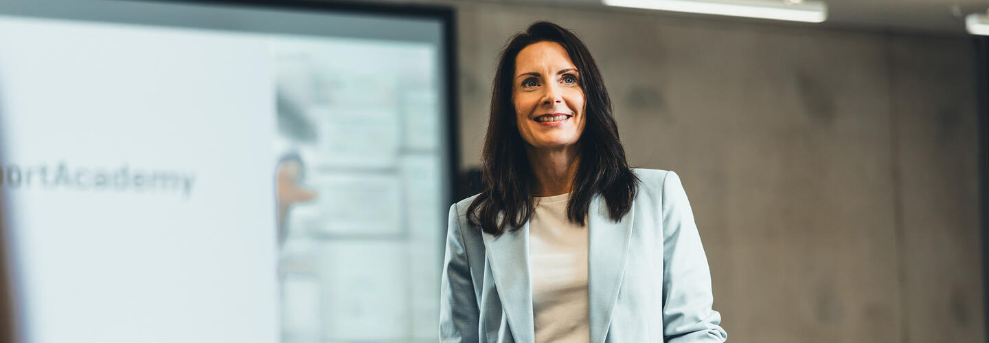 Die AirportAcademy am LabCampus Trainerin steht in einem Schulungsraum vor einer Leinwand.