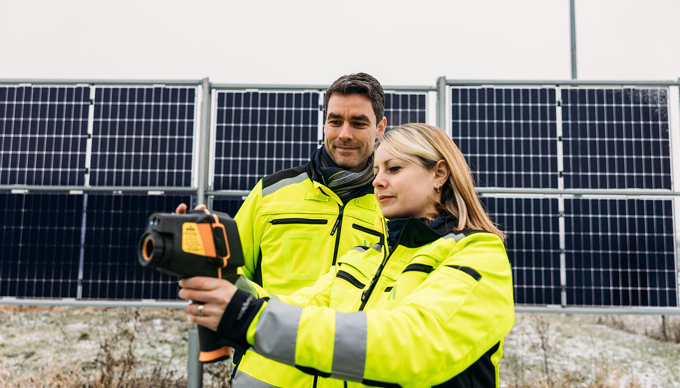 Energiemanagement am Flughafen München Zwei Personen in Warnjacken führen eine Messung mit einem Infrarotgerät vor einer Reihe von Photovoltaik-Modulen durch.