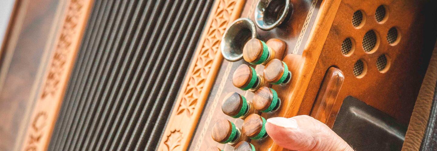 Oktoberfest Gewinnspiel 2025 Nahaufnahme einer traditionellen Ziehharmonika mit verzierten Holzelementen und sichtbaren Knöpfen, eine Hand spielt das Instrument.