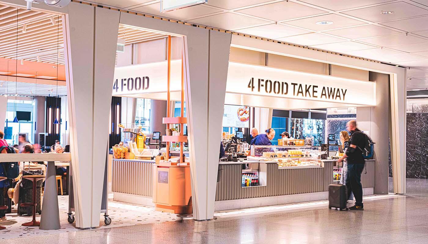 4 FOOD Take Away Theke 4 FOOD Take Away Theke mit einem Mitarbeiter hinter der Theke und zwei Kunden vor der Theke. Links im Bild ist der Sitzbereich des Restaurants 4 FOOD zu erkennen.