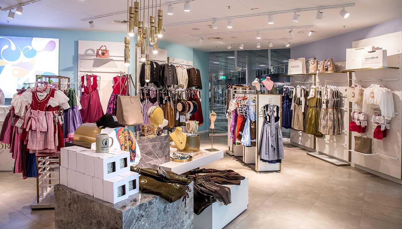 Trachtendealer Shop Innenansicht Die Innensicht des Trachtendealer Shops mit vielen verschiedenen Dirndl in unterschiedlichen Farben, Lederhosen, Jankern sowie Trachtenaccessoires. Die Dirndl hängen an Kleiderstangen im gesamten Shop, die Lederhosen liegen auf einem großen weißen Quader in der Mitte des Shops.