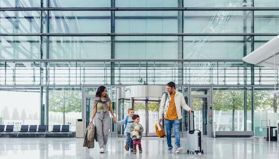 Traveling with Kids Mother and father with two young boys standing with travel luggage inside a modern airport building with glass facade in the background
