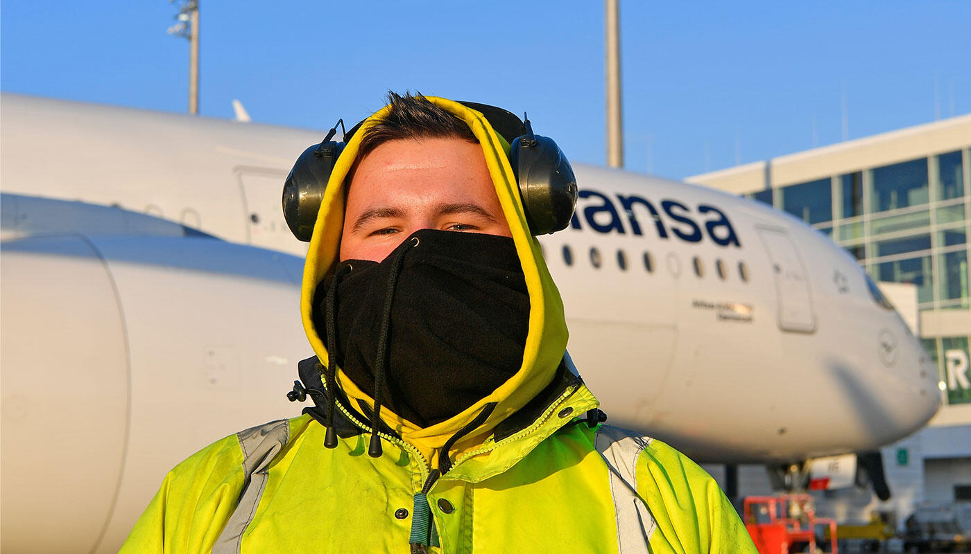Kälte am Flughafen München Mitarbeiter am Flughafen München in Warnjacke, mit Gehörschutz und Gesichtsmaske, steht bei eisigen Temperaturen vor einem geparkten Lufthansa-Flugzeug.