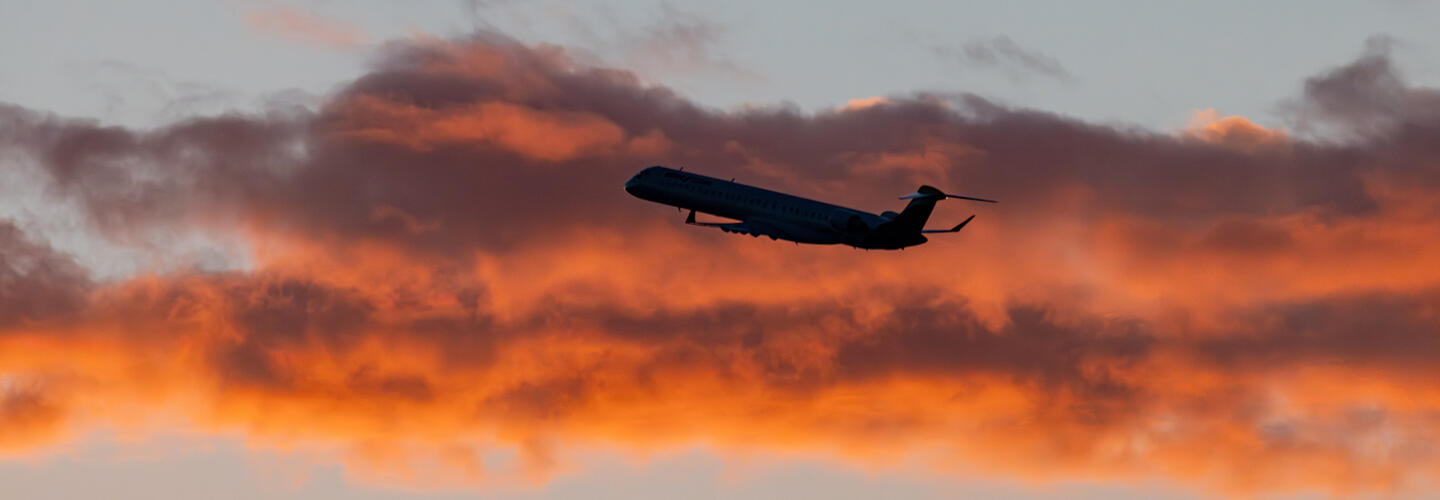 Flugzeug bei Sonnenuntergang Flugzeug steigt vor orange gefärbten Wolken bei Sonnenuntergang in den Himmel.