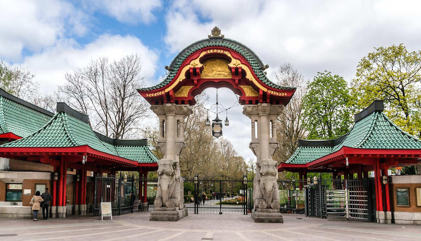 Elefantentor, Zoologischer Garten Berlin Haupteingang des Zoologischen Gartens Berlin, das Elefantentor. Zu sehen ist ein reich verziertes Tor mit zwei steinernen Elefanten und pagodenartigen Dächern links und rechts. Im Hintergrund sind Bäume. Der Himmel ist leicht bewölkt und blau.