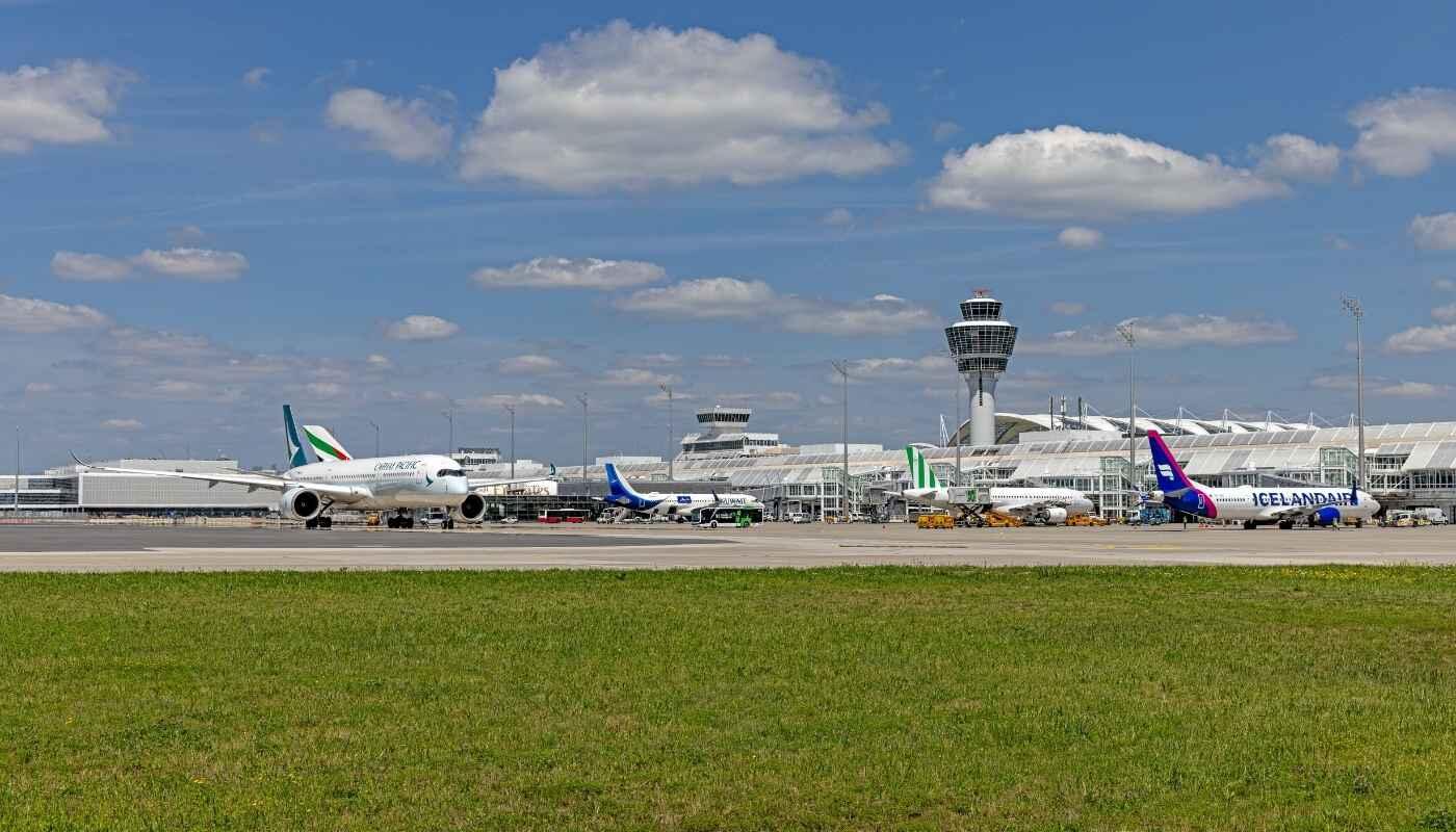 Neue Flugverbindungen ab München – Flughafen und Airlines Mehrere Flugzeuge verschiedener Airlines stehen auf dem Vorfeld des Flughafens München vor dem Tower. Die Szene symbolisiert neue Flugverbindungen und den Ausbau des internationalen Streckennetzes.