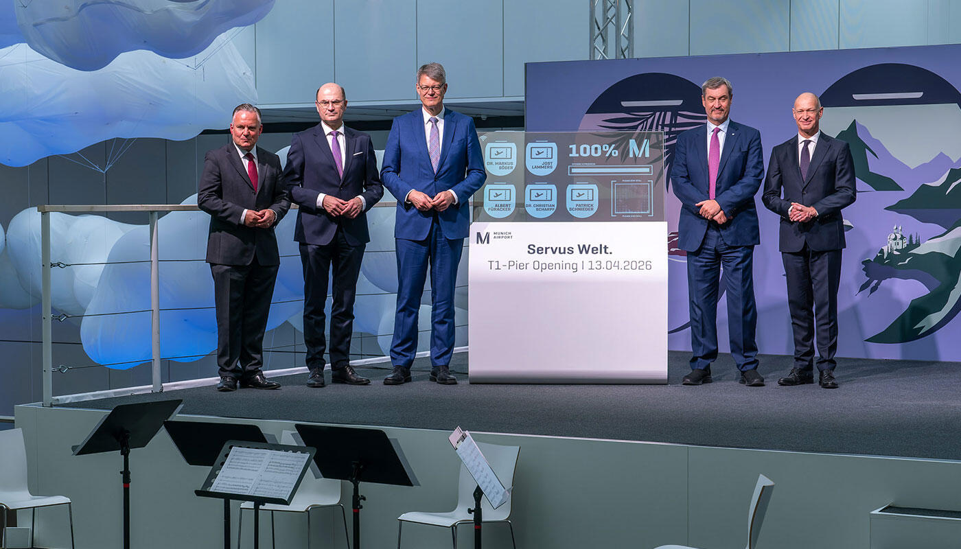 Grand Opening of Terminal 1 Pier at Munich Airport Five men are standing next to an OLED display that shows 100% and has opened the pier