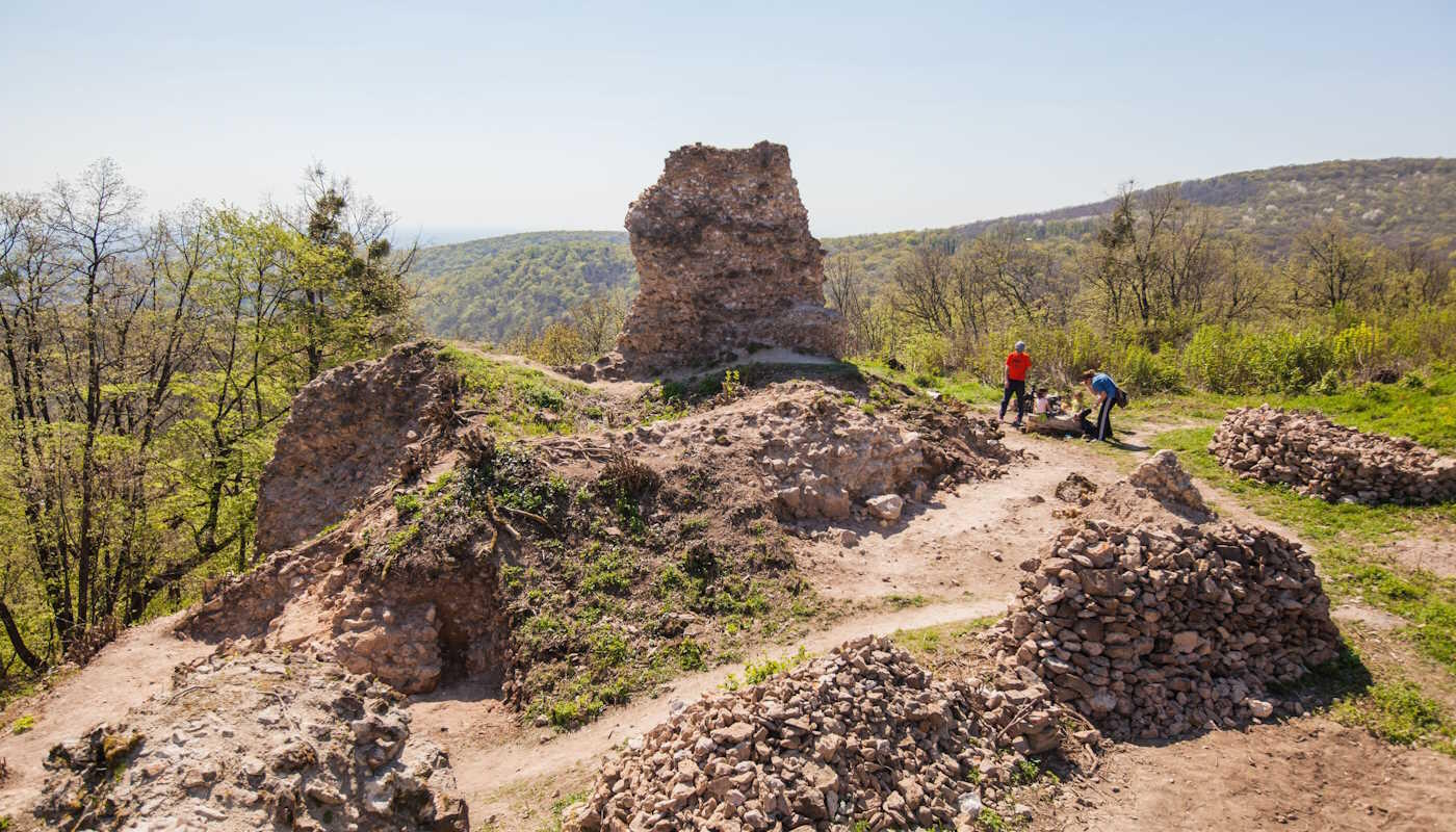 Fruška Gora Nationalpark, Serbien Die mittelalterlichen Ruinen des Vrdnik-Turms im Fruška Gora Nationalpark in Serbien, umgeben von bewaldeten Bergen und Wanderwegen. Zwei Menschen erkunden die steinernen Überreste der Anlage bei sonnigem Wetter.