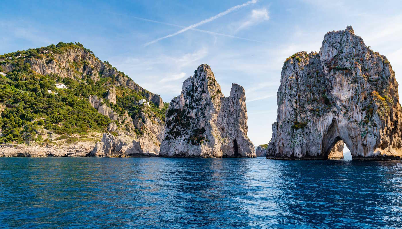 Faraglioni Felsen in Italein Das Felsformation Faraglioni di Capri vor der Insel Capri in Italie. Imposante Kalksteinfelsen, die steil aus dem tiefblauen Meer ragen. Besonders auffällig ist der große Felsen mit dem natürlichen Torbogen, durch den Boote hindurchfahren können. Die Landschaft wirkt wild, mediterran und sehr sonnig.