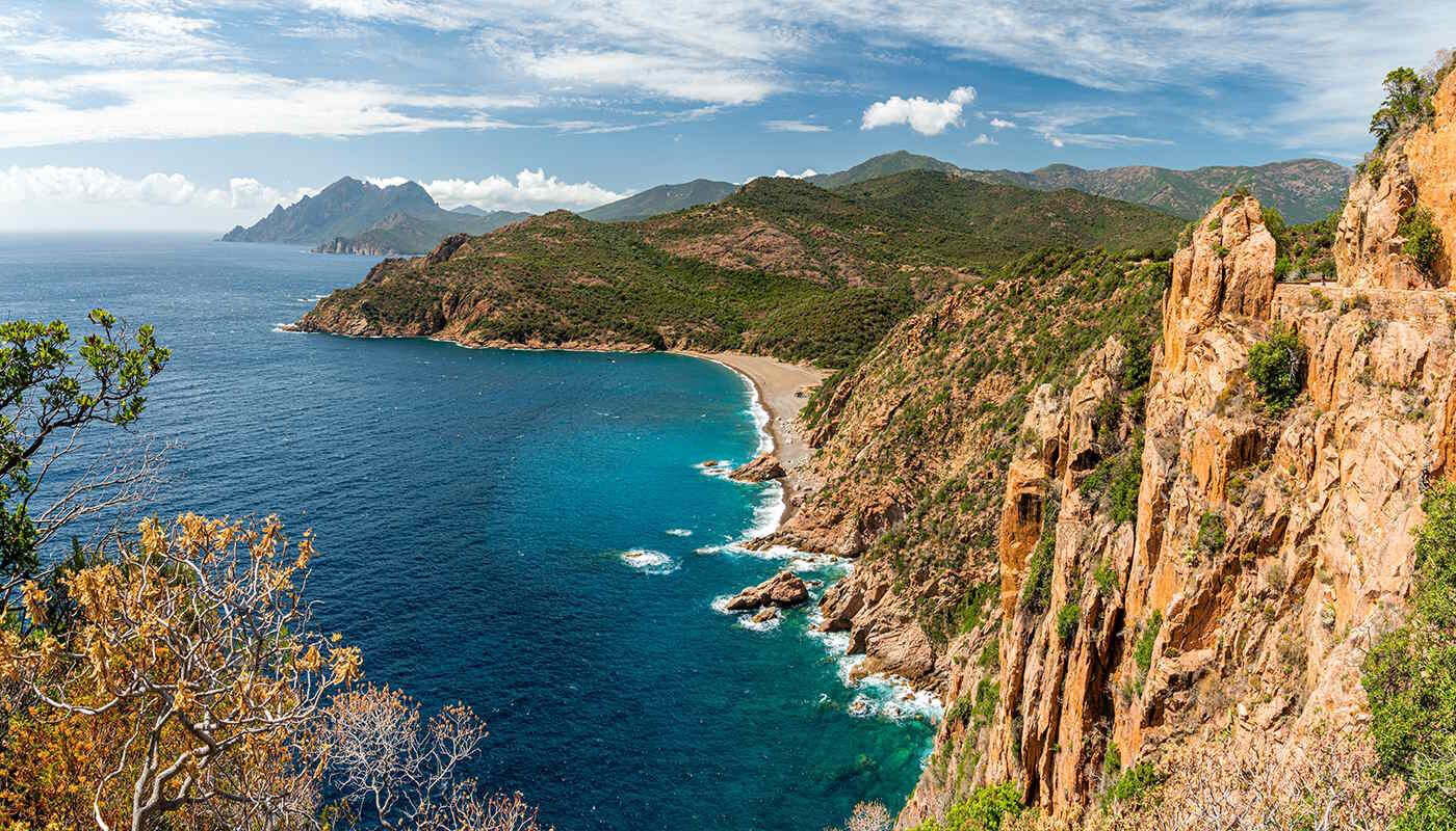 Calanques de Piana, Korsika, Frankreich Die Aufnahme zeigt die Calanques de Peana auf Korsika, eine steile, felsige Küstenlandschaft mit türkisblauem Meer und einer kleinen Bucht, umgeben von dicht bewachsenen Hügeln.