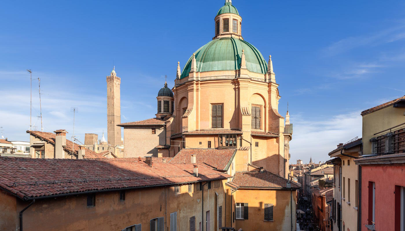 Santuario di Santa Maria della Vita in Bologna, Italien Das Bild zeigt die markante Kuppel des Santuario di Santa Maria della Vita über den charakteristischen ziegelgedeckten Dächern der Altstadt von Bologna. Im Hintergrund sind zudem einige der berühmten mittelalterlichen Türme der Stadt zu erkennen, die das historische Stadtbild prägen.