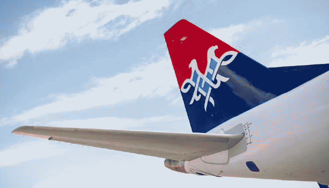 Leitwerk Air Serbia Der hintere Teil eines Flugzeugs von Air Serbia ist zu sehen. Das Leitwerk zeigt das farbige Logo der Airline. Der Himmel und Teile des Flughafens bilden den Hintergrund.