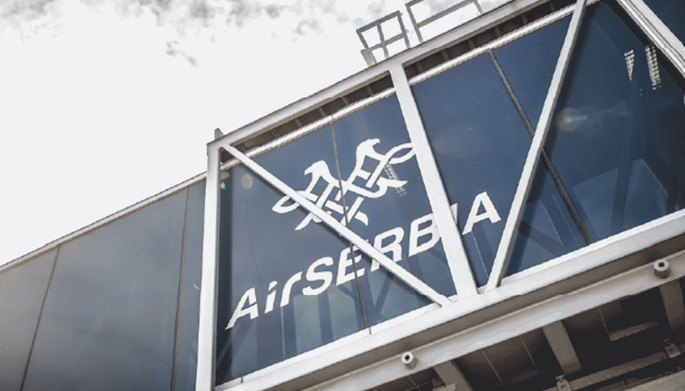 Flugsteig mit Air-Serbia-Branding Ein Flughafen-Gangway mit großer Glasfläche ist zu sehen. Darauf befindet sich das Logo und der Schriftzug „Air Serbia“. Die Konstruktion besteht aus Metallstreben und verbindet Terminal und Flugzeug.