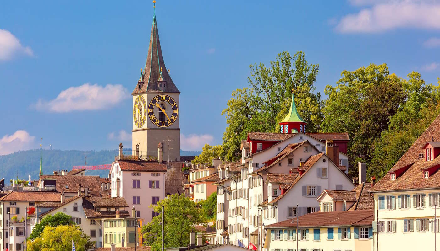 Ausblick auf Zürich, Schweiz Die Aufnahme zeigt die historische Altstadt von Zürich mit ihren charakteristischen Häusern und dem markanten Turm der Kirche St. Peter, dessen großes Zifferblatt zu den bekanntesten Wahrzeichen der Stadt zählt. Der Himmel ist klar und blau.