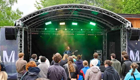Eine Musikerin begeistert das Publikum auf der Open-Air-Bühne des FünfSieben Festivals. Junge Besucherinnen und Besucher verfolgen den Live-Auftritt vor der stimmungsvoll beleuchteten Bühne und erleben gemeinsam einen unvergesslichen Moment voller Musik, Gemeinschaft und Festivalatmosphäre.